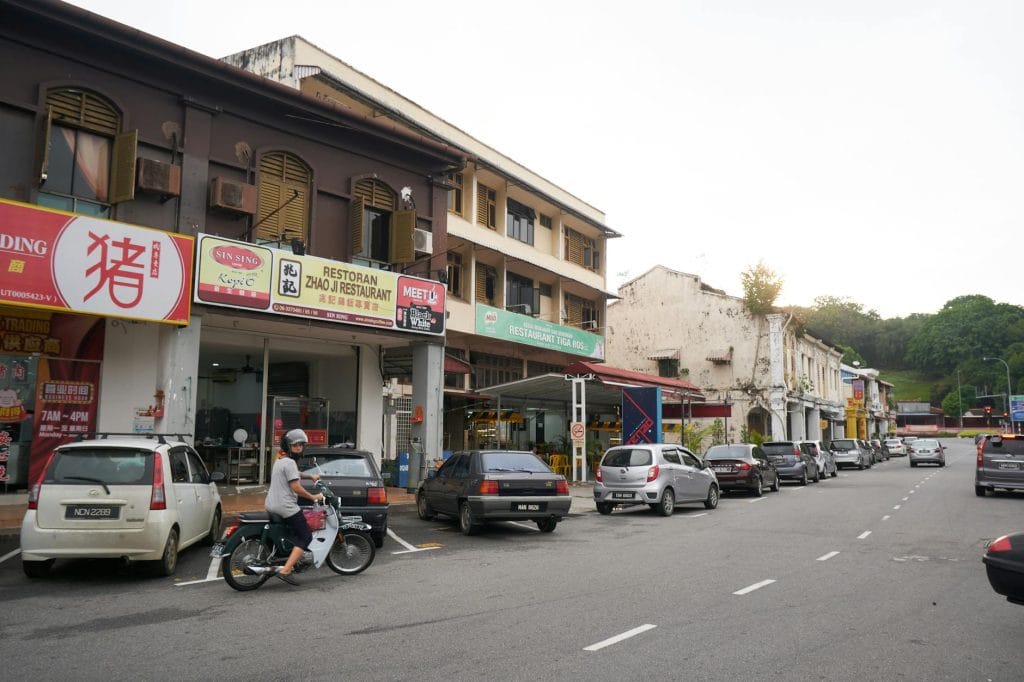 A lively city street with parked cars, motorbike, and shops in the afternoon light. komisyen ejen hartanah